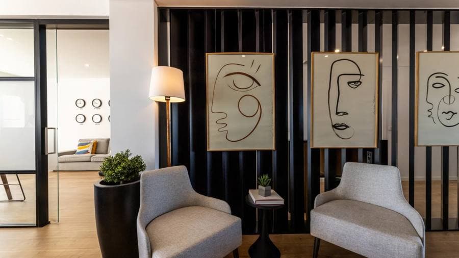 Salon de Reis & Pellicano avec fauteuils, tableaux sur un mur à lattes graphite et horloges mondiales en arrière-plan